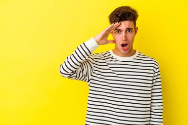 Kafkasyalı genç adam sarı arka planda izole edilmiş, uzaklara bakıyor ve elini alnına koyuyor..