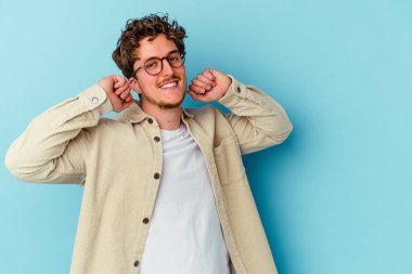 Gözlük takan genç beyaz adam mavi arka planda izole edilmiş, kollarını esnetiyor, rahat pozisyonda..