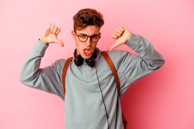 Pembe arka planda izole edilmiş genç bir öğrenci baş parmağını aşağı gösteriyor ve hoşlanmadığını ifade ediyor..