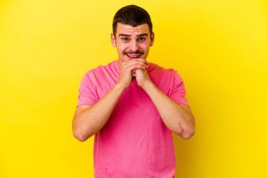 Sarı arka planda izole genç beyaz adam ellerini çenesinin altında tutuyor, mutlu bir şekilde yana bakıyor..