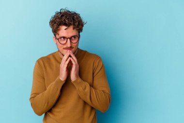 Gözlüklü genç beyaz adam mavi arka planda izole edilmiş. Aklında bir plan kuruyor..