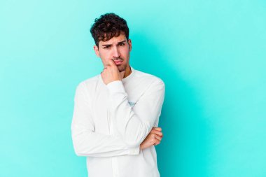 Kafkasyalı genç adam mavi arka planda izole edilmiş şüpheli, belirsiz, seni muayene ediyor..