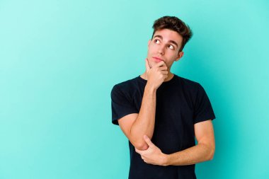 Mavi arka planda izole edilmiş genç beyaz adam rahatlamış bir şeyin fotokopi odasına baktığını düşünüyor..