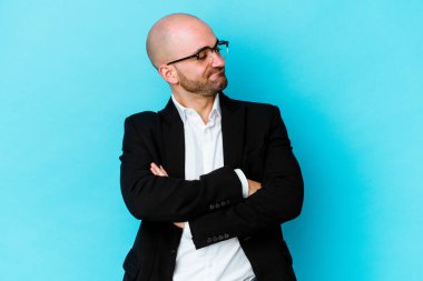 Genç, beyaz, kel bir adam mavi arka planda izole edilmiş. Amaçlarına ve amaçlarına ulaşma hayali kuruyor.