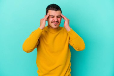 Genç beyaz adam mavi arka planda izole edilmiş tapınaklara dokunuyor ve başı ağrıyor..