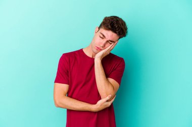 Mavi arka planda izole edilmiş, sıkılmış, yorgun ve dinlenmeye ihtiyacı olan genç beyaz bir adam..