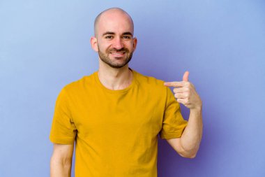 Mor arka planda izole olmuş genç, beyaz kel bir adam gömlek fotokopi alanını elle işaret ediyor, gururlu ve kendinden emin