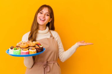Sarı arka planda izole edilmiş genç pasta şefi kadın bir avuç içinde fotokopi alanı ve belinde bir el daha gösteriyor..