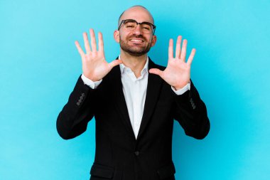 Genç beyaz tenli kel adam mavi arka planda izole edilmiş. 10 numarayı elleriyle gösteriyor..