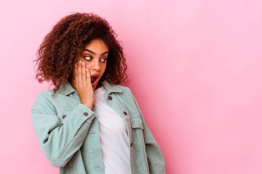 Genç Afrikalı Amerikalı kadın pembe arka planda izole edilmiş. Gördüğü bir şey yüzünden şoka uğruyor..