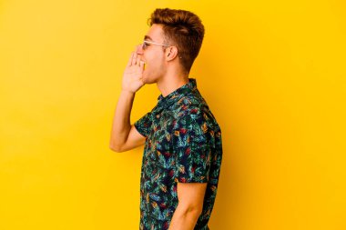 Sarı arka planda izole edilmiş Hawaii gömleği giyen genç, beyaz bir adam bağırıyor ve ağzı açık bir şekilde avuç içi tutuyor..