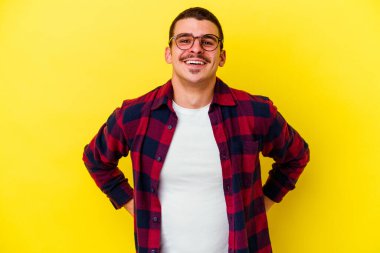 Sarı arka planda izole genç beyaz adam ellerini kalçasında tutuyor..