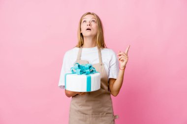 Genç Rus fırıncı kadın elinde lezzetli bir pasta, ağzı açık ve üst tarafı işaret ediyor..