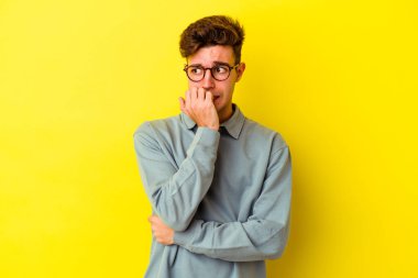Sarı arka planda izole edilmiş, tırnak yiyen, gergin ve endişeli genç bir beyaz adam..