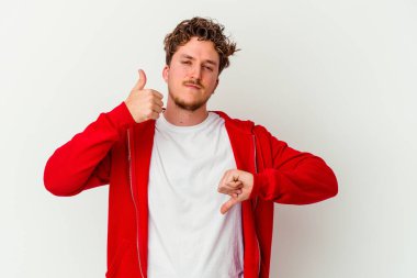 Beyaz arka planda izole edilmiş genç beyaz bir adam baş parmaklarını aşağı ve yukarı kaldırıyor, zor seçim konsepti