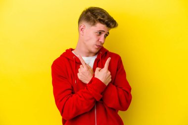 Sarı arka planda izole genç beyaz adam, iki seçenek arasında seçim yapmaya çalışıyor.