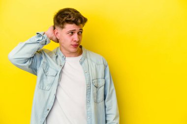 Kafkasyalı genç adam sarı arka planda izole edilmiş kafasının arkasına dokunuyor, düşünüyor ve bir seçim yapıyor..