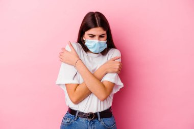 Virüs maskesi takan beyaz bir kadın. Pembe arka planda izole edilmiş. Düşük ateş ya da hastalık nedeniyle soğuyor..