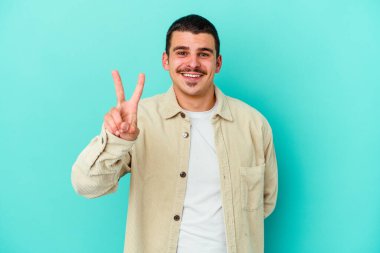 Mavi arka planda izole edilmiş genç beyaz adam iki numarayı parmaklarıyla gösteriyor..