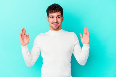 Kafkasyalı genç adam mavi arka planda izole edilmiş. Elinde işaret parmaklarıyla küçük bir şey tutuyor, gülümsüyor ve kendinden emin..