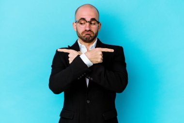 Mavi arka plan noktalarında izole genç beyaz adam iki seçenek arasında seçim yapmaya çalışıyor..