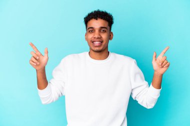 Genç Afro-Amerikalı kıvırcık adam mavi üzerine izole edilmiş, farklı fotokopi alanlarını gösteriyor, birini seçiyor, parmaklarıyla gösteriyor..