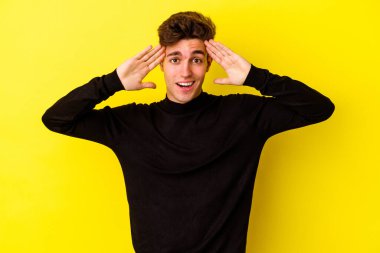 Sarı arka planda izole genç beyaz adam hoş bir sürpriz alıyor, heyecanlı ve el kaldırıyor..