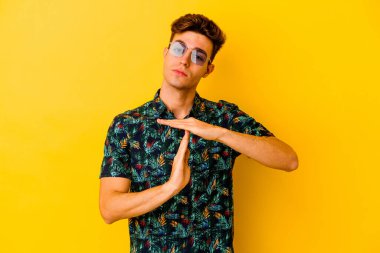 Hawaii tişörtü giyen beyaz bir genç sarı arka planda izole edilmiş bir şekilde bir mola hareketi gösteriyor..