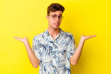 Kafkasyalı genç adam sarı arka planda izole edilmiş. Kafası karışmış ve omuz silkiyor. Kopya alanını tutmak için..