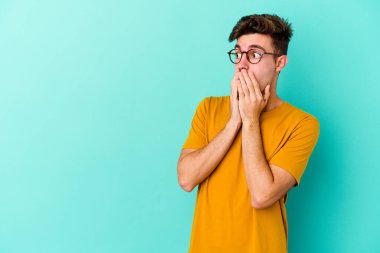 Kafkasyalı genç adam mavi arka planda izole edilmiş. Düşünceli bir şekilde ağzıyla ağzını kapatan bir fotokopi odasına bakıyor..