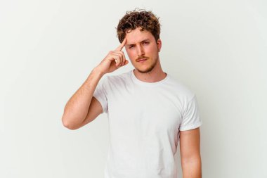 Beyaz arka planda izole edilmiş genç beyaz bir adam şakağı parmağıyla işaret ediyor, düşünüyor ve bir göreve odaklanıyor..