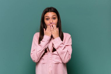 Mavi arka planda izole edilmiş genç bir Hintli kadın şok olmuş, elleriyle ağzını kapatmış, yeni bir şey keşfetmek için sabırsızlanıyor..