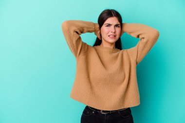 Kafkasyalı genç bir kadın mavi arka planda izole edilmiş kafasının arkasına dokunuyor, düşünüyor ve bir seçim yapıyor..