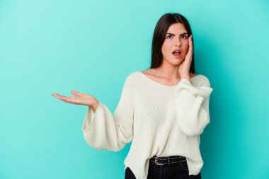 Mavi arka planda izole edilmiş genç beyaz kadın, avuç içinin fotokopi alanını tutmaktan etkilenmiş..