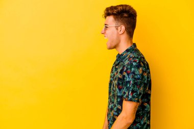 Sarı arka planda izole edilmiş Hawaii gömleği giyen genç beyaz bir adam fotokopi odasına doğru bağırıyor.