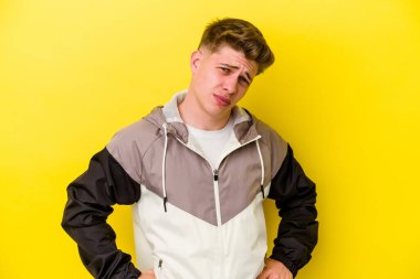 Sarı arka planda izole edilmiş genç beyaz adam hoşnutsuzca kaşlarını çatmış, kollarını kavuşturmuş..