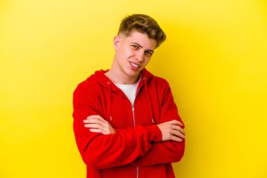 Sarı arka planda izole edilmiş genç beyaz adam kendini güvende hissediyor, kararlılıkla kollarını kavuşturuyor..