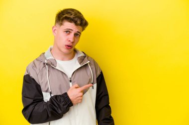 Sarı arka planda izole edilmiş genç beyaz adam gülümsüyor ve boş alanda bir şeyler gösteriyor..