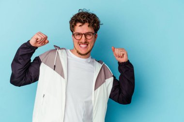 Mavi arka planda izole edilmiş gözlüklü genç beyaz adam zaferden sonra yumruğunu kaldırıyor, kazanan konsept..