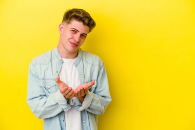 Sarı arka planda izole edilmiş genç, beyaz bir adam. Dudaklarını kıvırıyor, avuç içlerini tutuyor ve hava öpücüğü yolluyor..