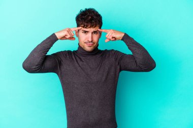 Kafkasyalı genç adam mavi arka planda izole edilmiş bir göreve odaklanmış, parmaklarını işaret ediyor..