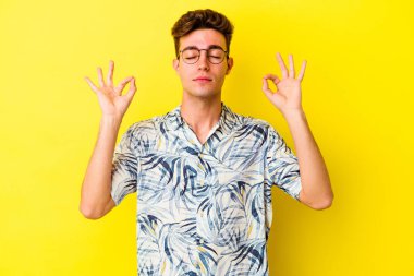 Sarı arka planda izole edilmiş genç beyaz adam sıkı çalışma gününden sonra rahatlıyor. Yoga yapıyor..