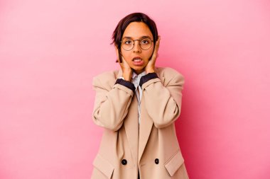 Genç iş kadını, pembe arka planda izole edilmiş kulakları kulaklarıyla kapatarak yüksek sesle ses duymamaya çalışıyor..