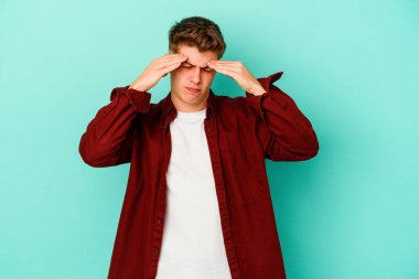 Kafkasyalı genç bir adam mavi arka planda izole edilmiş, başı ağrıyor, yüzüne dokunuyor..