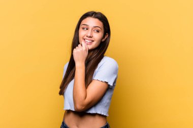 Sarı arka planda izole edilmiş genç Hintli kadın rahatlamış fotokopi odasına bakan bir şey düşünüyor..