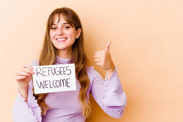 Young caucasian woman holding a Refugees welcome placard isolated smiling and raising thumb up