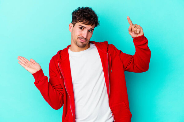 Молодой кавказский человек изолирован на синем фоне, держа и показывая товар под рукой.