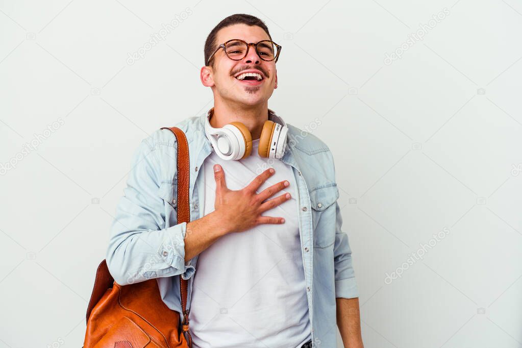 Young caucasian student man listening to music isolated on white background laughs out loudly keeping hand on chest.