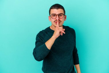 Mavi arka planda izole edilmiş genç beyaz bir adam ya sır saklıyor ya da sessizlik istiyor..