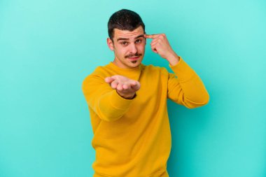 Kafkasyalı genç adam mavi arka planda izole edilmiş ve elinde bir ürün tutuyor..